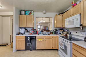 Kitchen featuring white appliances, a textured ceiling, light brown cabinetry, and hanging light fixtures