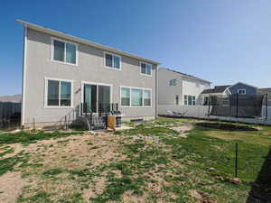 Rear view of property featuring a trampoline, a fenced backyard, stucco siding, and a lawn