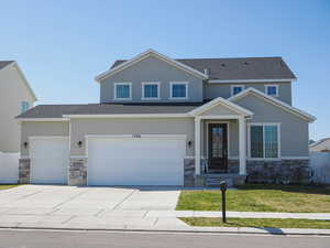 View of front of home with driveway, stone siding, fence, and stucco siding