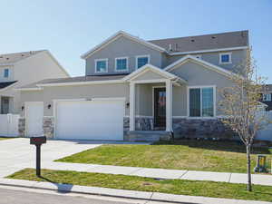 View of front facade with concrete driveway, stucco siding, stone siding, a front lawn, and fence