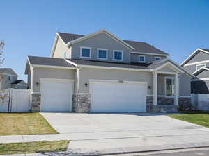 Craftsman-style home featuring concrete driveway, stucco siding, stone siding, and fence