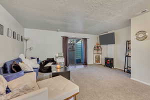 Living room featuring carpet, a textured ceiling, and a wood stove