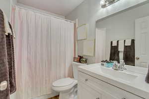 Bathroom featuring curtained shower, toilet, and vanity