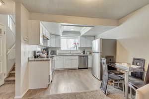 Kitchen with white cabinets, stainless steel appliances, light wood-type flooring, a tray ceiling, and crown molding