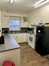 Kitchen with black refrigerator, sink, white cabinets, and white range with electric stovetop