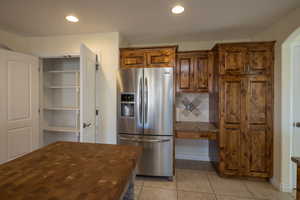 Kitchen with butcher block counters, backsplash, stainless steel fridge with ice dispenser, and light tile patterned floors