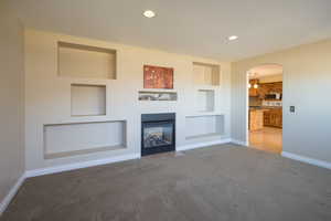 Unfurnished living room featuring built in shelves and light carpet