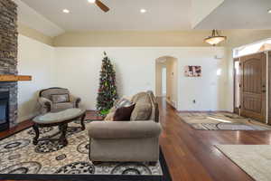 Living room featuring ceiling fan, dark wood-type flooring, a fireplace, and lofted ceiling