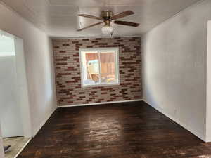 Unfurnished room featuring brick wall, ceiling fan, and dark hardwood / wood-style flooring