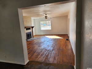 Unfurnished living room featuring ceiling fan, dark wood-type flooring, and a fireplace