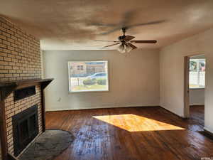 Unfurnished living room with a fireplace, dark wood-type flooring, a textured ceiling, and ceiling fan