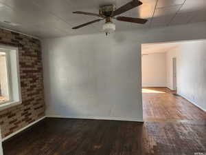 Spare room with ceiling fan, brick wall, and dark hardwood / wood-style flooring