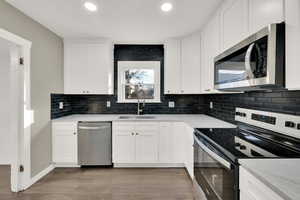 Kitchen featuring sink, backsplash, white cabinets, and appliances with stainless steel finishes