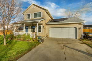 View of front of property with a garage, a front yard, a porch, and solar panels