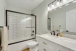 Full bathroom featuring vanity, toilet, combined bath / shower with glass door, and hardwood / wood-style flooring