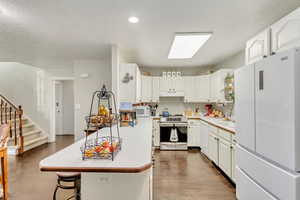 Kitchen featuring white cabinetry, white appliances, a center island, a breakfast bar, and a skylight