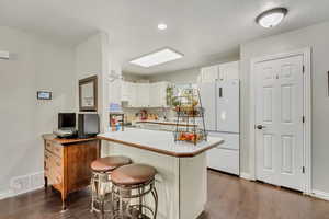 Kitchen with white cabinets, a center island, dark wood-type flooring, white fridge, and a breakfast bar