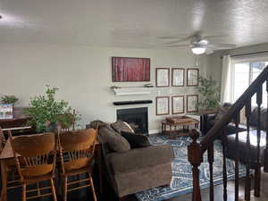 Living room featuring ceiling fan, carpet flooring, a textured ceiling, and a tiled fireplace