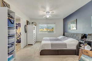 Bedroom featuring a textured ceiling, a walk in closet, a closet, ceiling fan, and light colored carpet