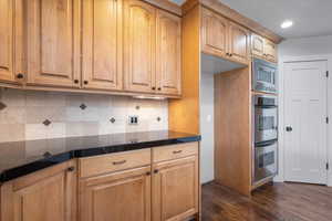 Kitchen with dark wood-type flooring, appliances with stainless steel finishes, and decorative backsplash