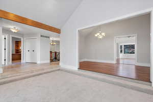 Unfurnished living room with beam ceiling, high vaulted ceiling, light colored carpet, and an inviting chandelier