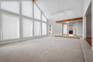 Unfurnished living room featuring light carpet, track lighting, high vaulted ceiling, and beamed ceiling