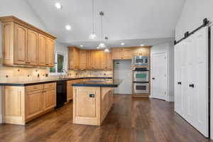 Kitchen with pendant lighting, lofted ceiling, sink, black appliances, and a barn door