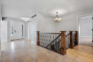 Entrance foyer featuring light tile patterned flooring, a textured ceiling, and a notable chandelier