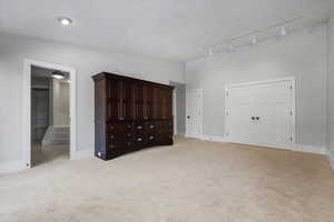 Unfurnished bedroom featuring light colored carpet, ensuite bathroom, vaulted ceiling, and a textured ceiling