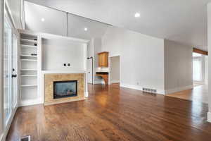 Unfurnished living room featuring high vaulted ceiling, wood-type flooring, a tile fireplace, and a textured ceiling