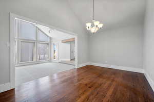 Empty room with an inviting chandelier, high vaulted ceiling, and hardwood / wood-style floors