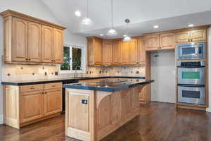 Kitchen with sink, a center island, black appliances, decorative light fixtures, and vaulted ceiling