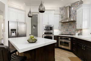 Kitchen featuring backsplash, white cabinets, wall chimney range hood, a breakfast bar area, and stainless steel appliances