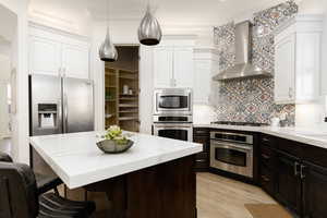 Kitchen with a kitchen bar, appliances with stainless steel finishes, tasteful backsplash, white cabinetry, and wall chimney exhaust hood