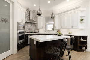 Kitchen with a center island, wall chimney exhaust hood, white cabinetry, stainless steel appliances, and sink