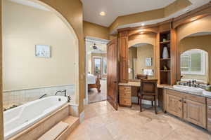 Bathroom with ceiling fan, tiled tub, and vanity