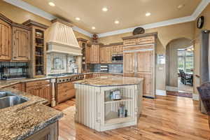 Kitchen with custom exhaust hood, backsplash, a center island, light hardwood / wood-style floors, and built in appliances