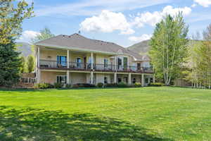 Back of house with a balcony, a lawn, and a mountain view