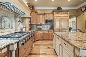 Kitchen featuring built in appliances, custom exhaust hood, light stone countertops, and decorative backsplash