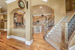 Kitchen with crown molding, stainless steel microwave, light stone countertops, light hardwood / wood-style floors, and decorative backsplash