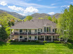 Back of house featuring a lawn, a deck with mountain view, and a patio