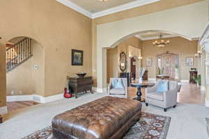 Carpeted living room featuring crown molding and an inviting chandelier