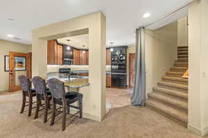 Kitchen with kitchen peninsula, sink, light tile patterned floors, light stone countertops, and a breakfast bar