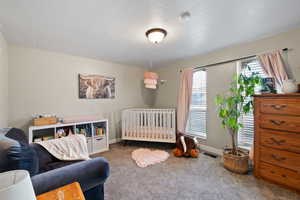 Carpeted bedroom with radiator heating unit, a crib, and a textured ceiling