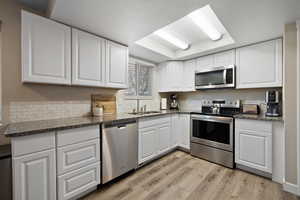 Kitchen featuring appliances with stainless steel finishes, white cabinets, light wood-type flooring, sink, and a tray ceiling