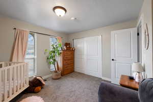 Bedroom with a textured ceiling, carpet flooring, a closet, and a nursery area