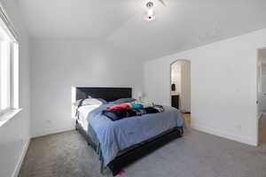 Carpeted bedroom with connected bathroom and lofted ceiling