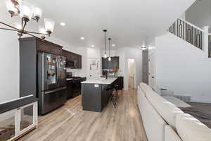 Kitchen with a kitchen breakfast bar, dark brown cabinetry, pendant lighting, an island with sink, and stainless steel appliances