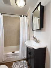 Full bathroom with hardwood / wood-style flooring, vanity, shower / tub combo, toilet, and a textured ceiling