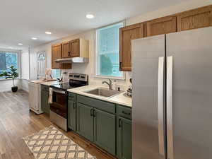 Kitchen featuring appliances with stainless steel finishes, sink, a textured ceiling, and light hardwood / wood-style floors